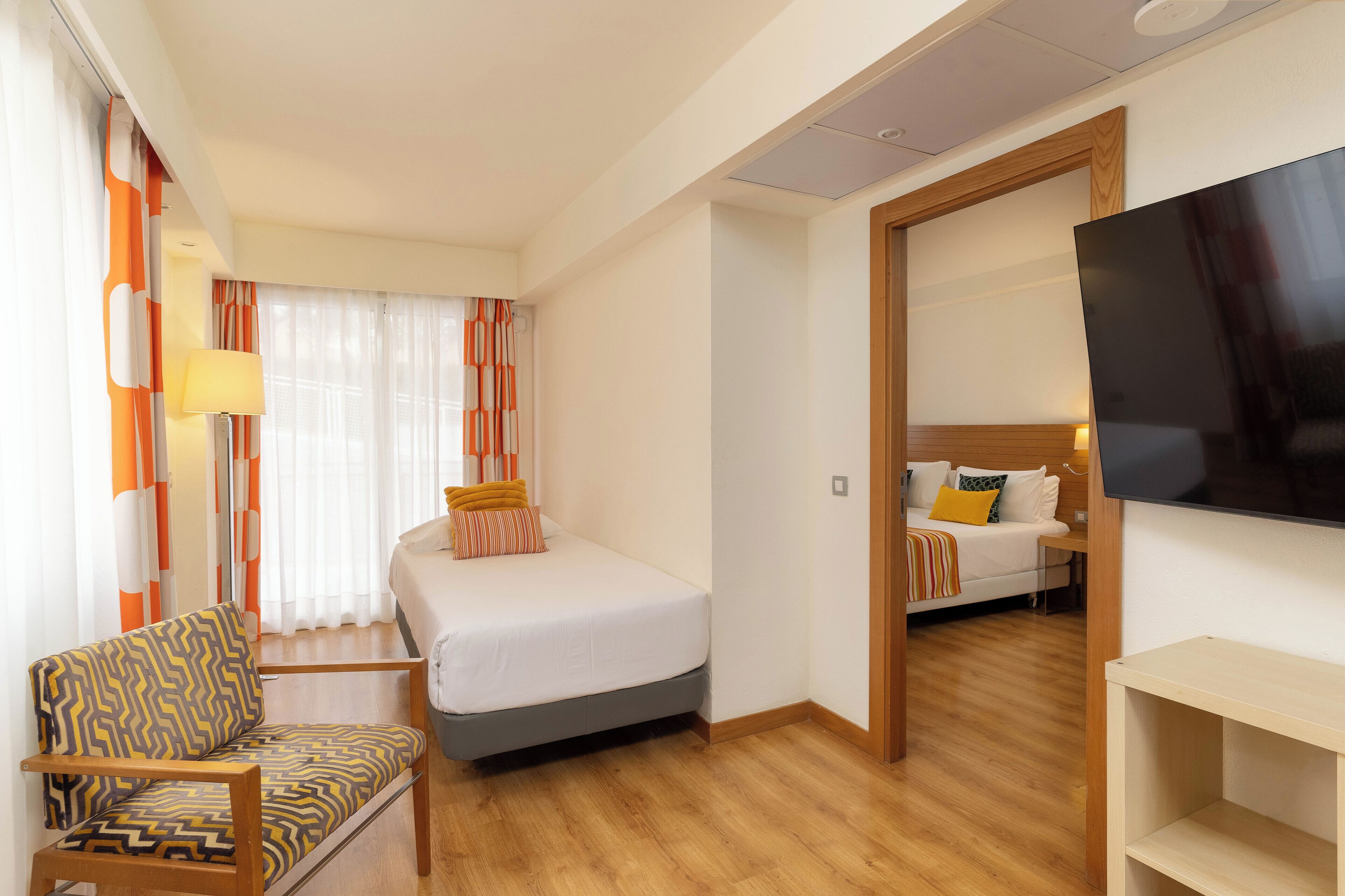 A hotel room with a bed, a chair, a TV, and a wooden floor.