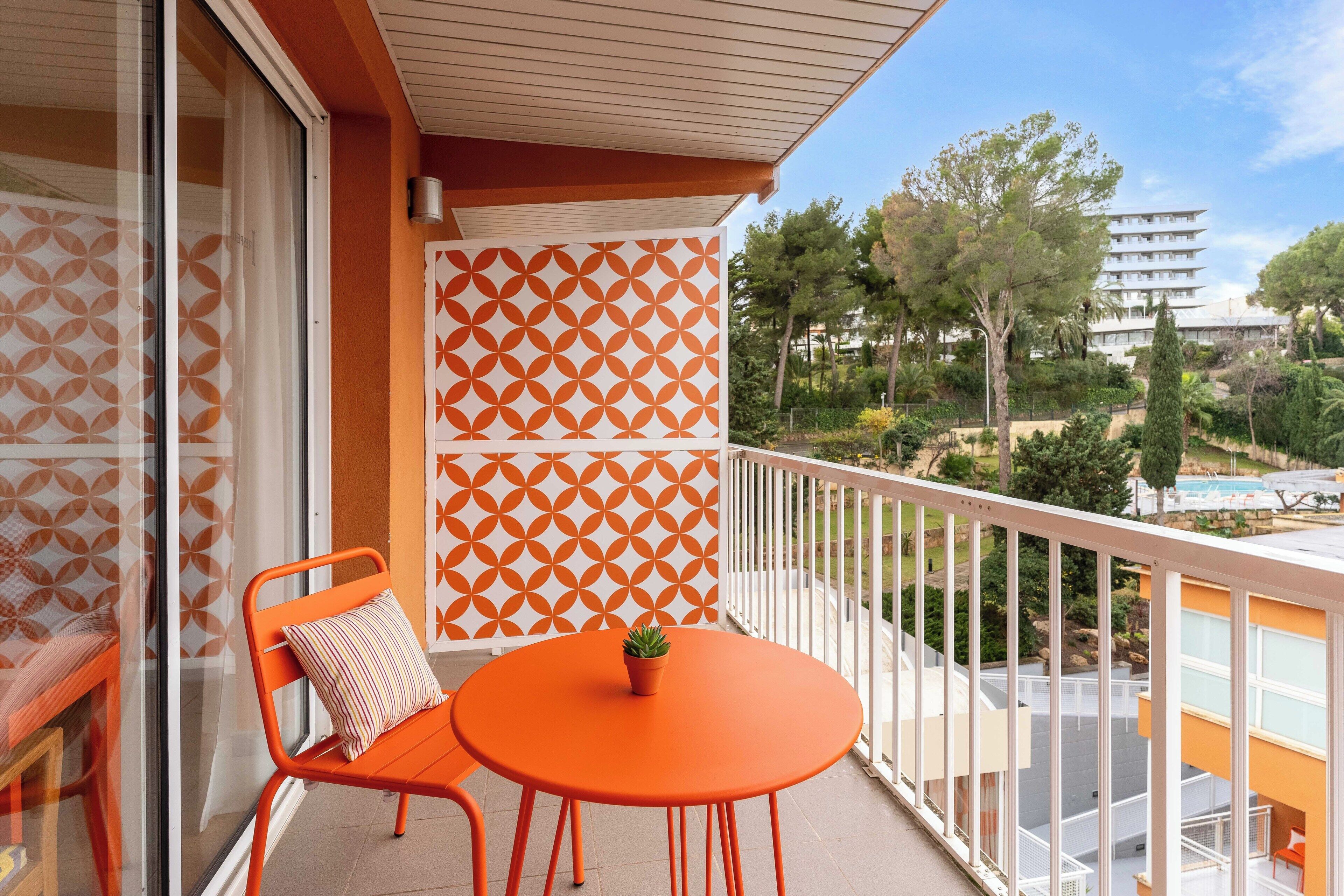A balcony with orange furniture, a patterned wall, and a view of a building and trees.
