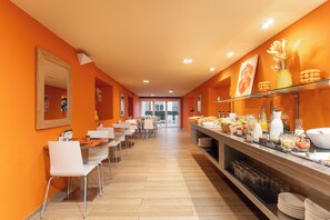 A bright orange dining area with multiple tables and chairs, a buffet counter with various food items, and a large mirror on the wall. - Hotel Hesperia Mallorca (Palma de Mallorca)