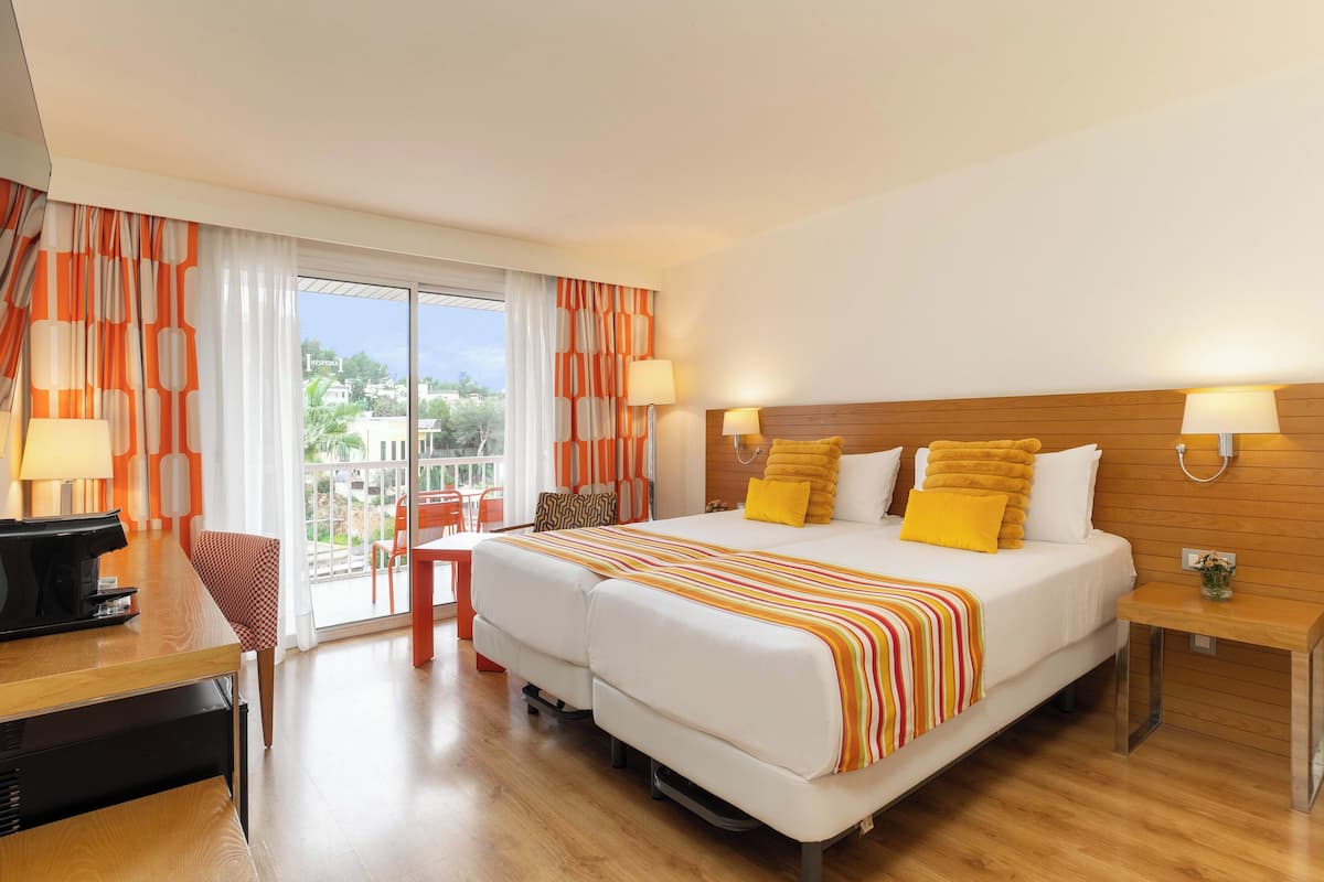 A hotel room with a large bed, two bedside tables, a desk with a chair, and a view of the outdoors.