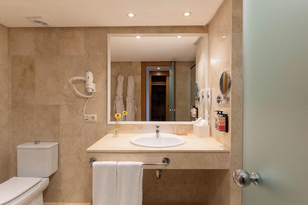 Un baño con inodoro, lavabo, espejo, toallero y secador de pelo.