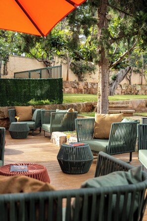 An outdoor seating area with wicker furniture and a large orange umbrella. - Hotel Hesperia Mallorca (Palma de Mallorca)