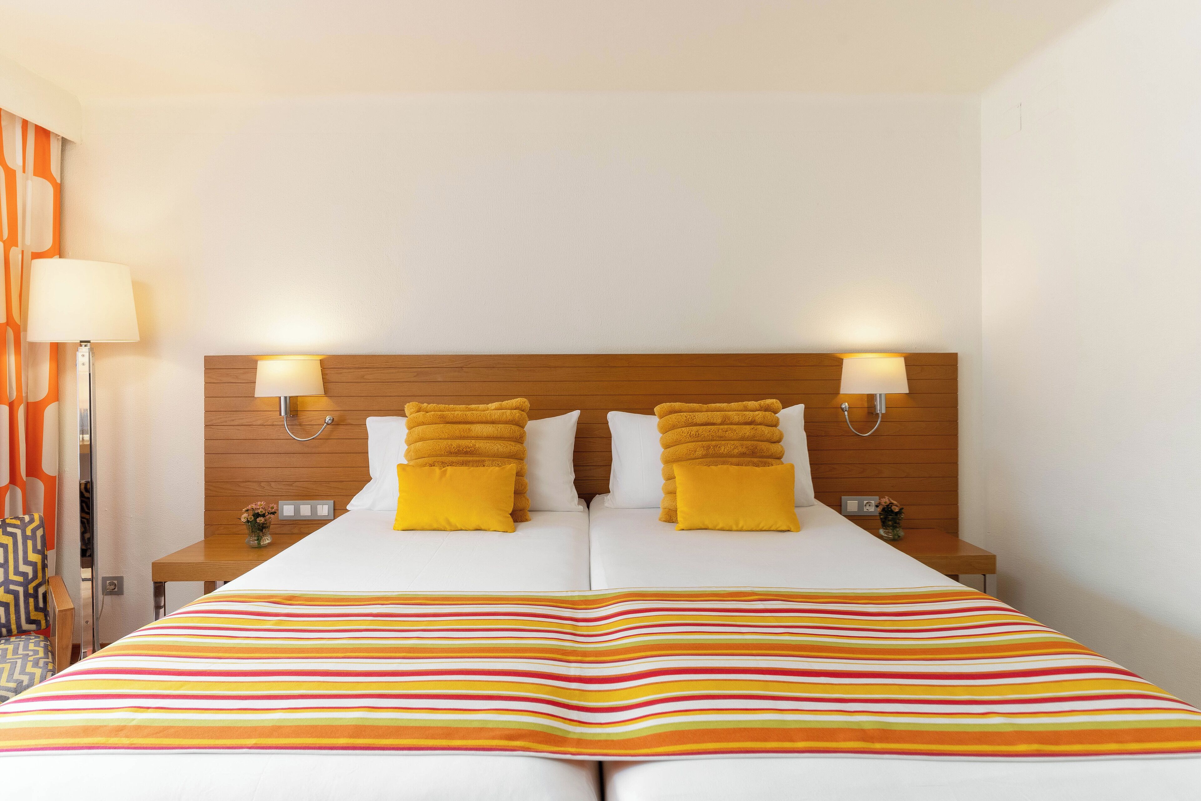 A double bed with a striped bedspread, two bedside lamps, and a wooden headboard.