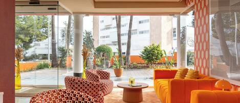 Un salón moderno con asientos estampados y una mesa de centro, con ventanas amplias que ofrecen vistas al exterior.