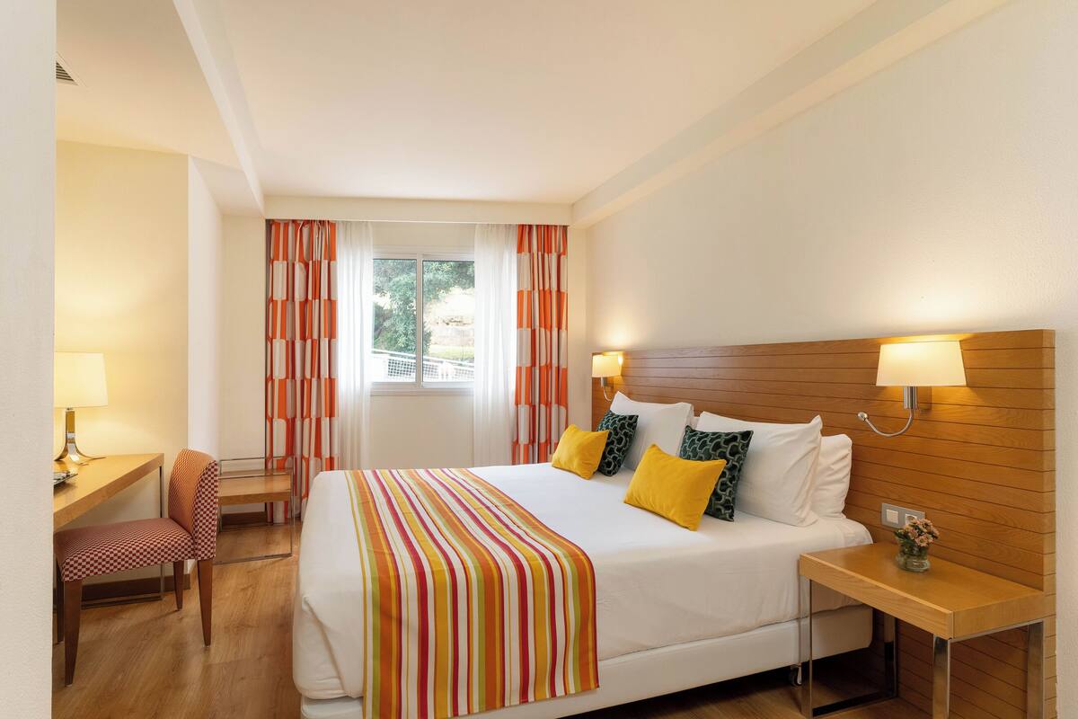 A hotel room with a bed, bedside tables, a desk, and a chair.