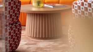 Una sala de estar moderna con una mesa de centro redonda de madera, sofá naranja con cojines amarillos y almohadas decorativas estampadas.