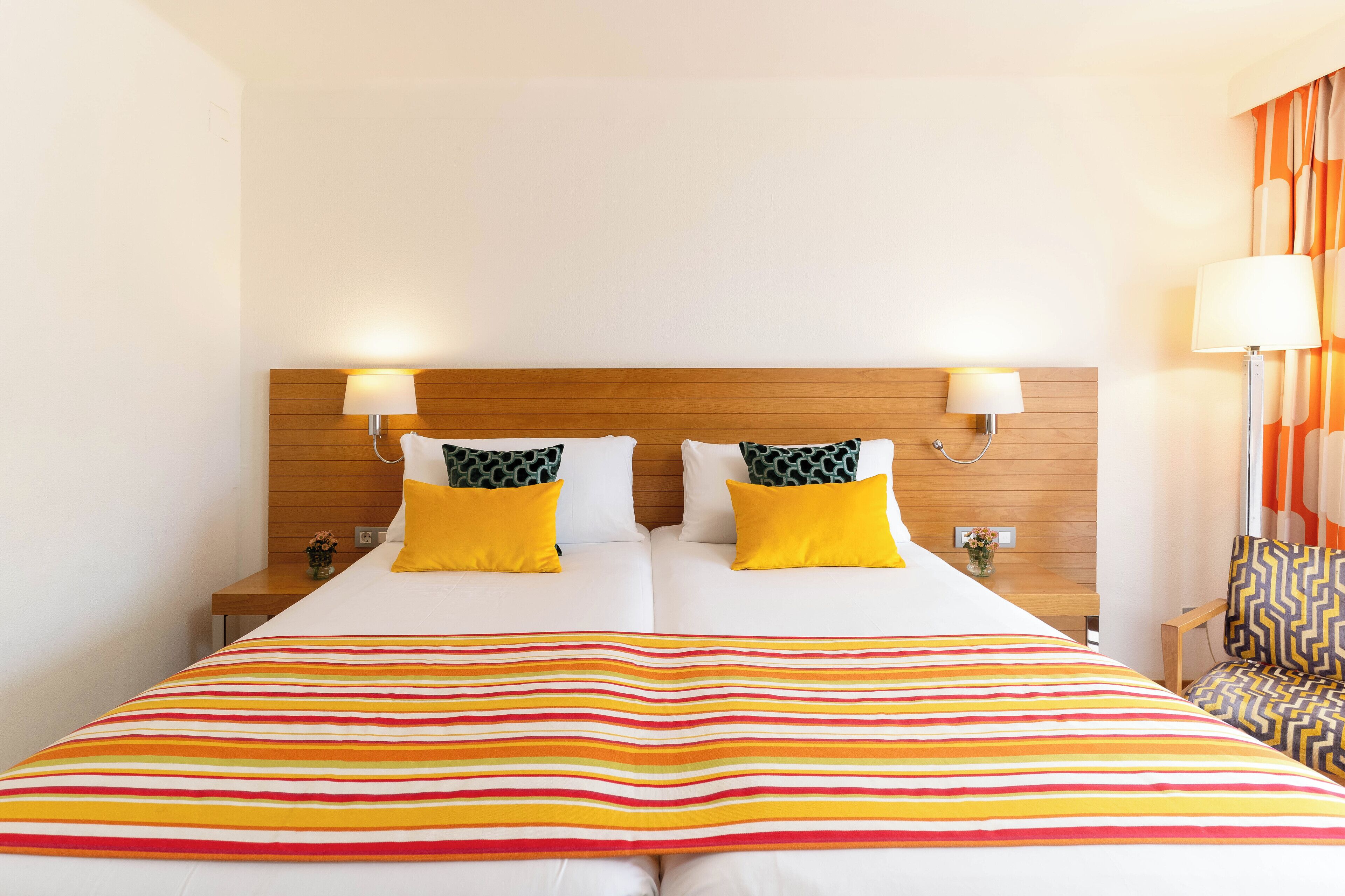 A hotel room with a large bed, two bedside lamps, a wooden headboard, and a striped bedspread.