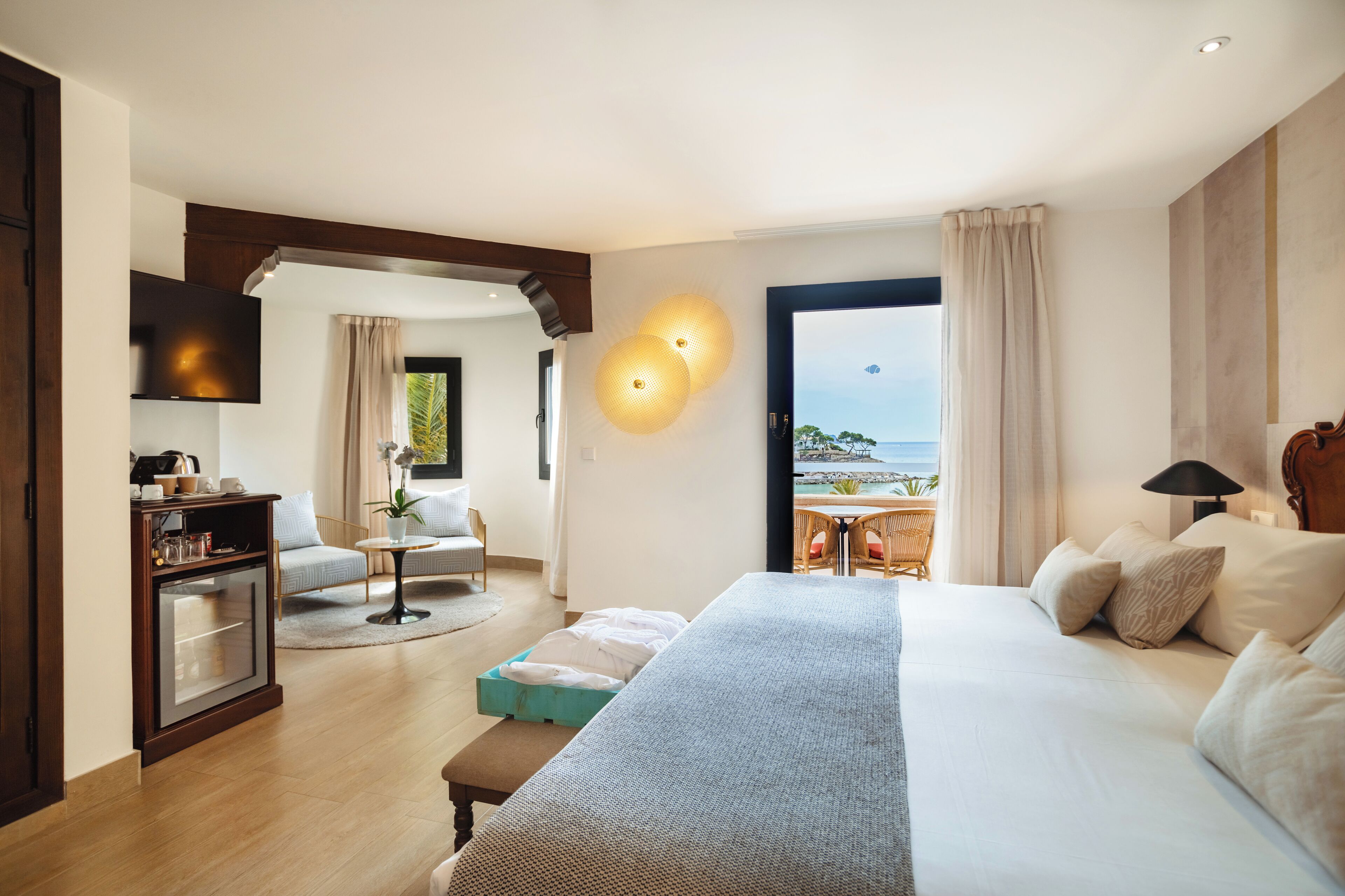 A hotel room with a large bed, a desk, a TV, and a view of the sea.