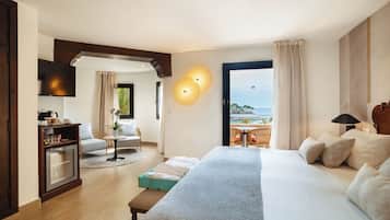 A hotel room with a large bed, a desk, a TV, and a view of the sea.