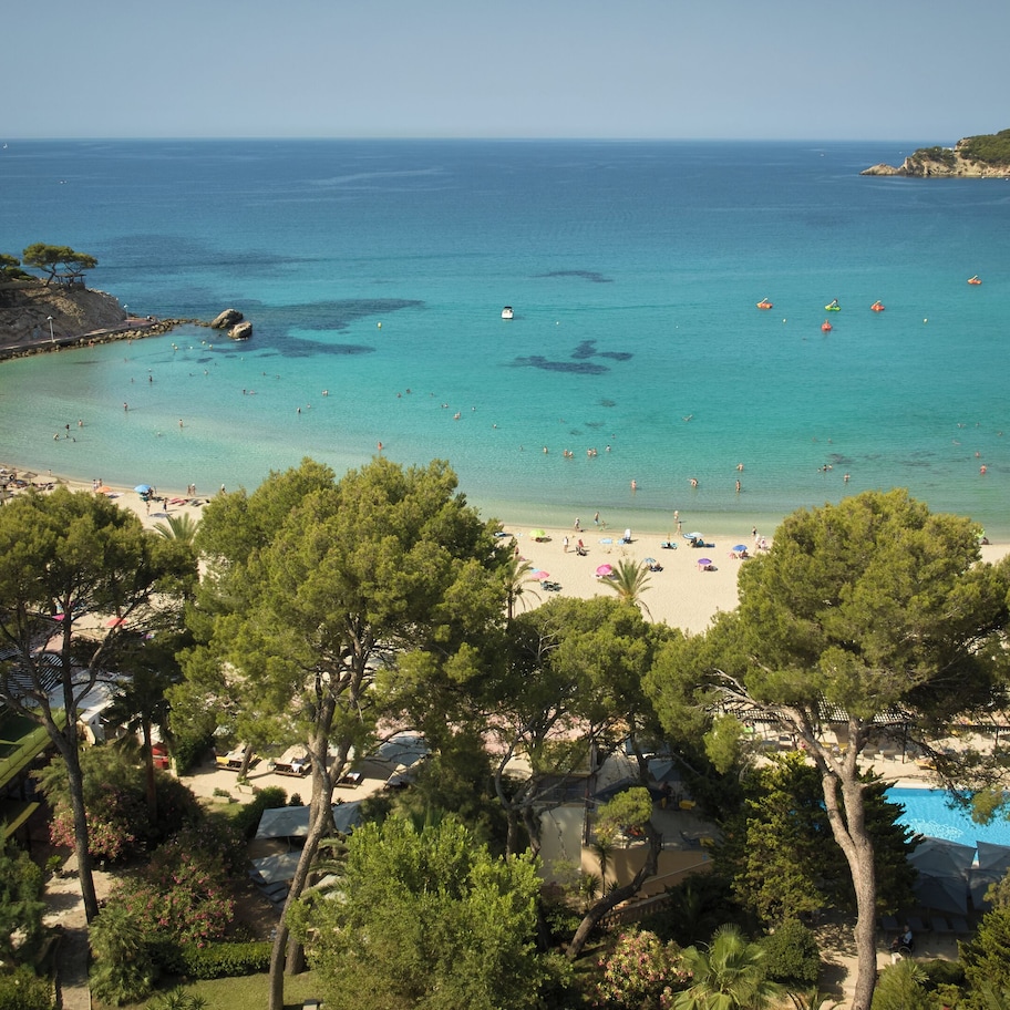A coastal resort with a beach, swimming pool, and lush greenery.