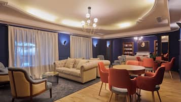 A spacious living room with a beige sofa, red chairs, a round wooden table, and a chandelier.