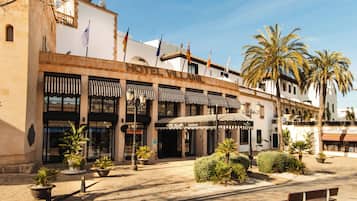 Un hotel con entrada principal, mesas al aire libre y palmeras.