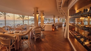 A restaurant with tables set for dining, wicker chairs, and a wine display. - Secrets Mallorca Villamil Resort & Spa - Adults Only (Calvia)