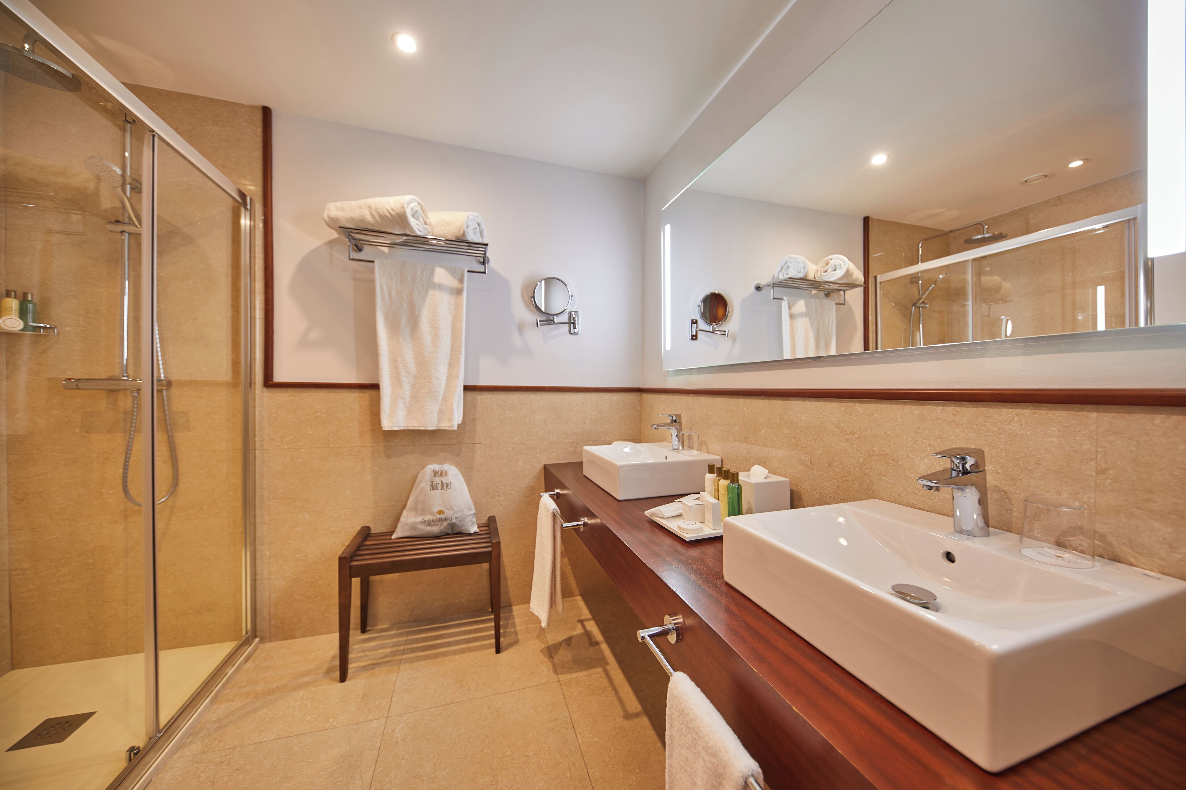 A modern bathroom with a glass-enclosed shower, two sinks, a vanity, and a large mirror.