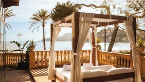 A four-poster bed with a canopy, positioned on a balcony with a view of the sea and mountains. - Secrets Mallorca Villamil Resort & Spa - Adults Only (Calvia)