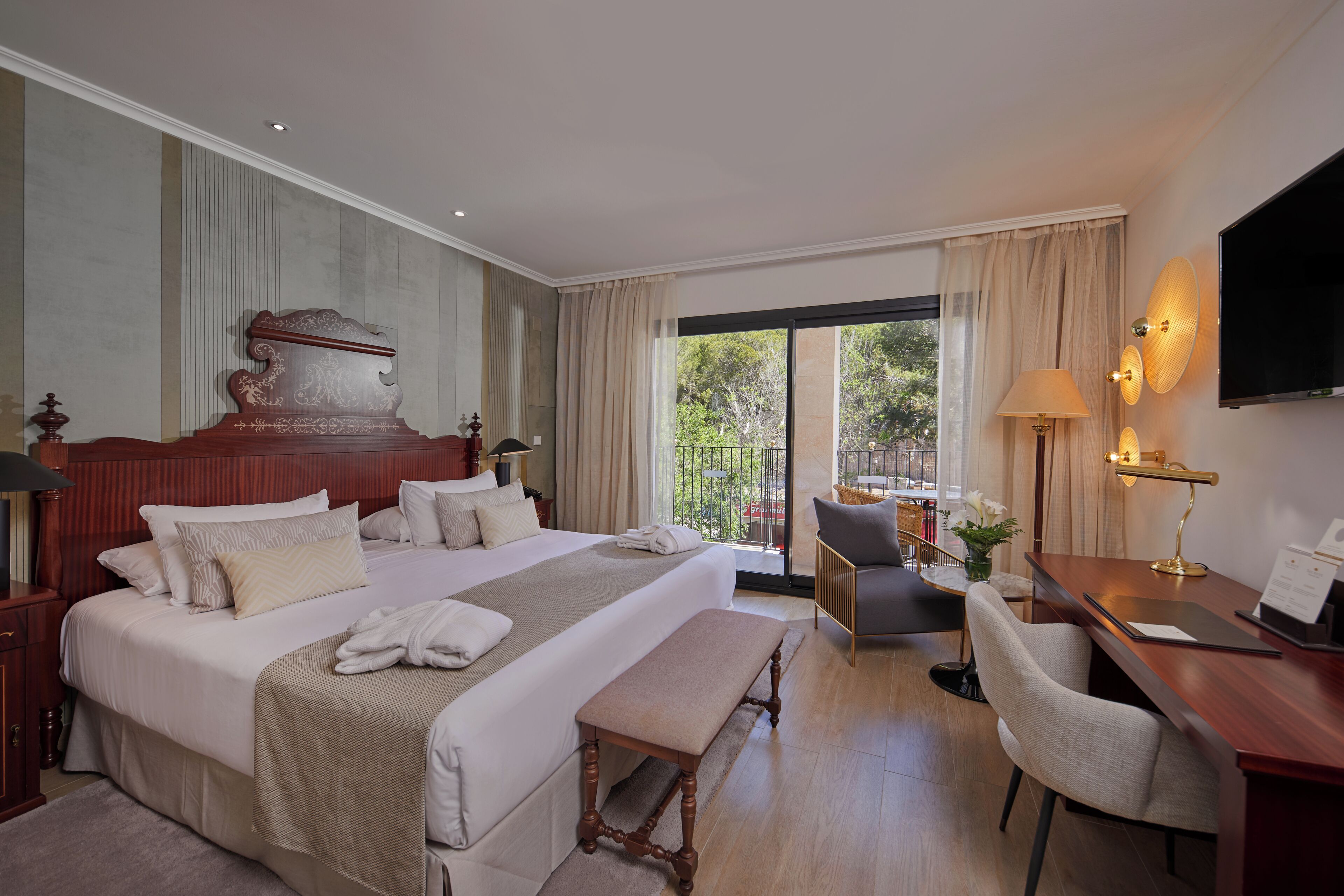 A hotel room with a large bed, a desk with a chair, a television, and a balcony with a view.
