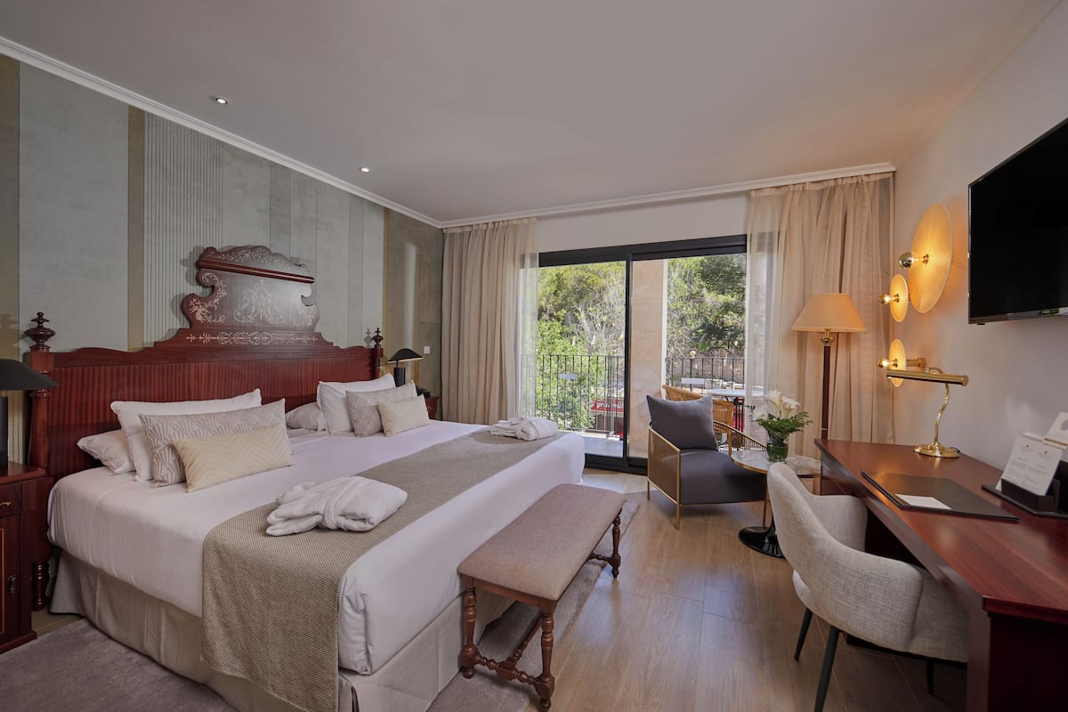 Habitación de hotel con una cama grande, un escritorio con silla, televisor y un balcón con vistas.