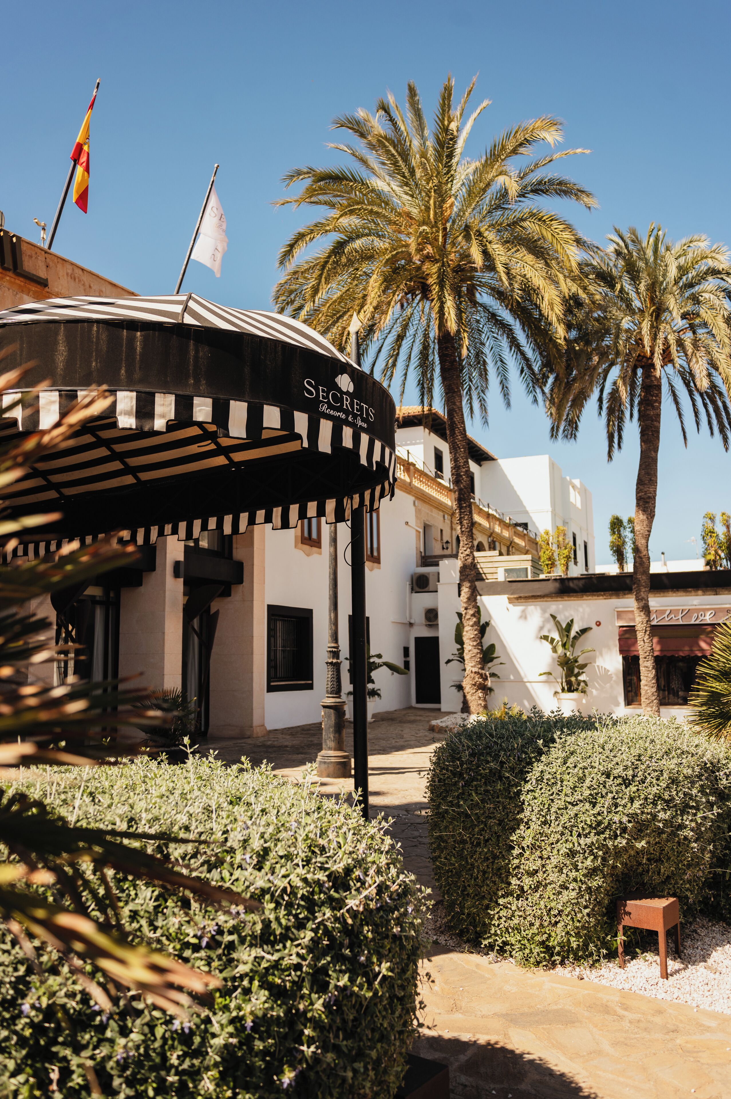 Un edificio con toldo a rayas identificado como "Secret's Bistro & Bar" y palmeras al fondo.