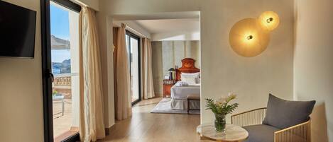 A hotel room with a bed, a TV, a table with a vase, and a chair. There is a view of the outside through the window.