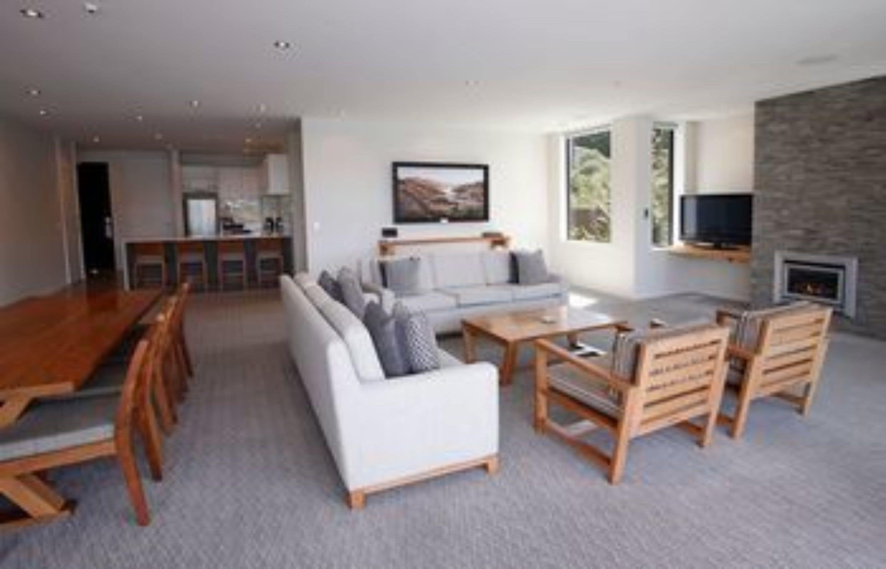 A modern living room with a sofa, coffee table, and wooden chairs. There is a fireplace and a television mounted on the wall.