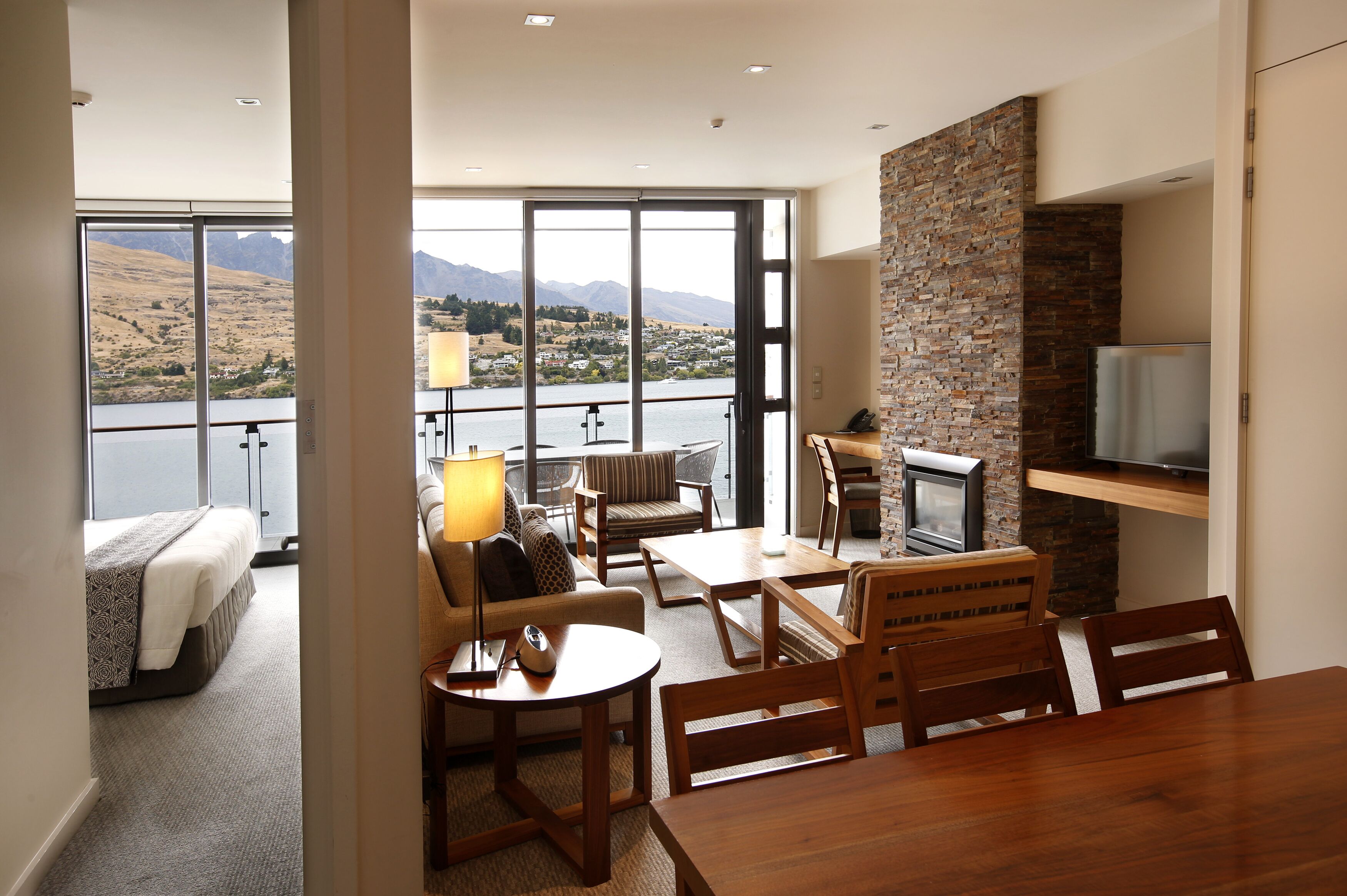 A modern hotel room with a balcony, a dining area, and a TV.