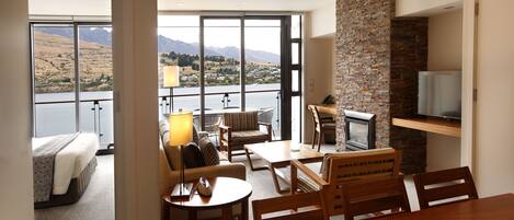 A modern hotel room with a balcony, a dining area, and a TV.
