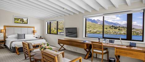 A modern bedroom with a bed, desk, and large windows offering a mountain view.