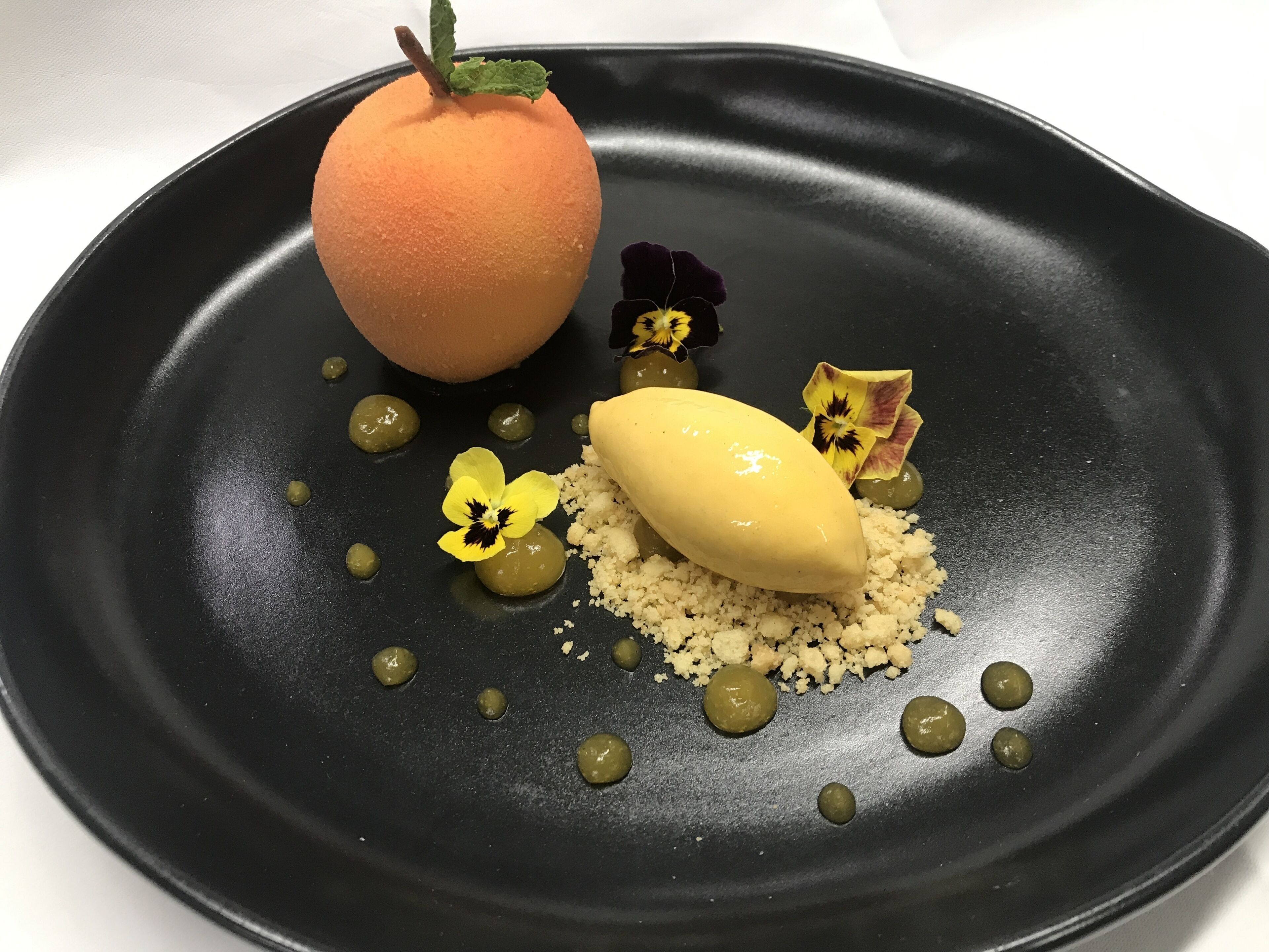 Une assiette de dessert avec une pêche, un fruit jaune, et de petites fleurs.