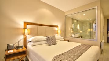 Habitación de hotel con una cama grande, lámparas de noche, un teléfono y un espejo que refleja el baño.