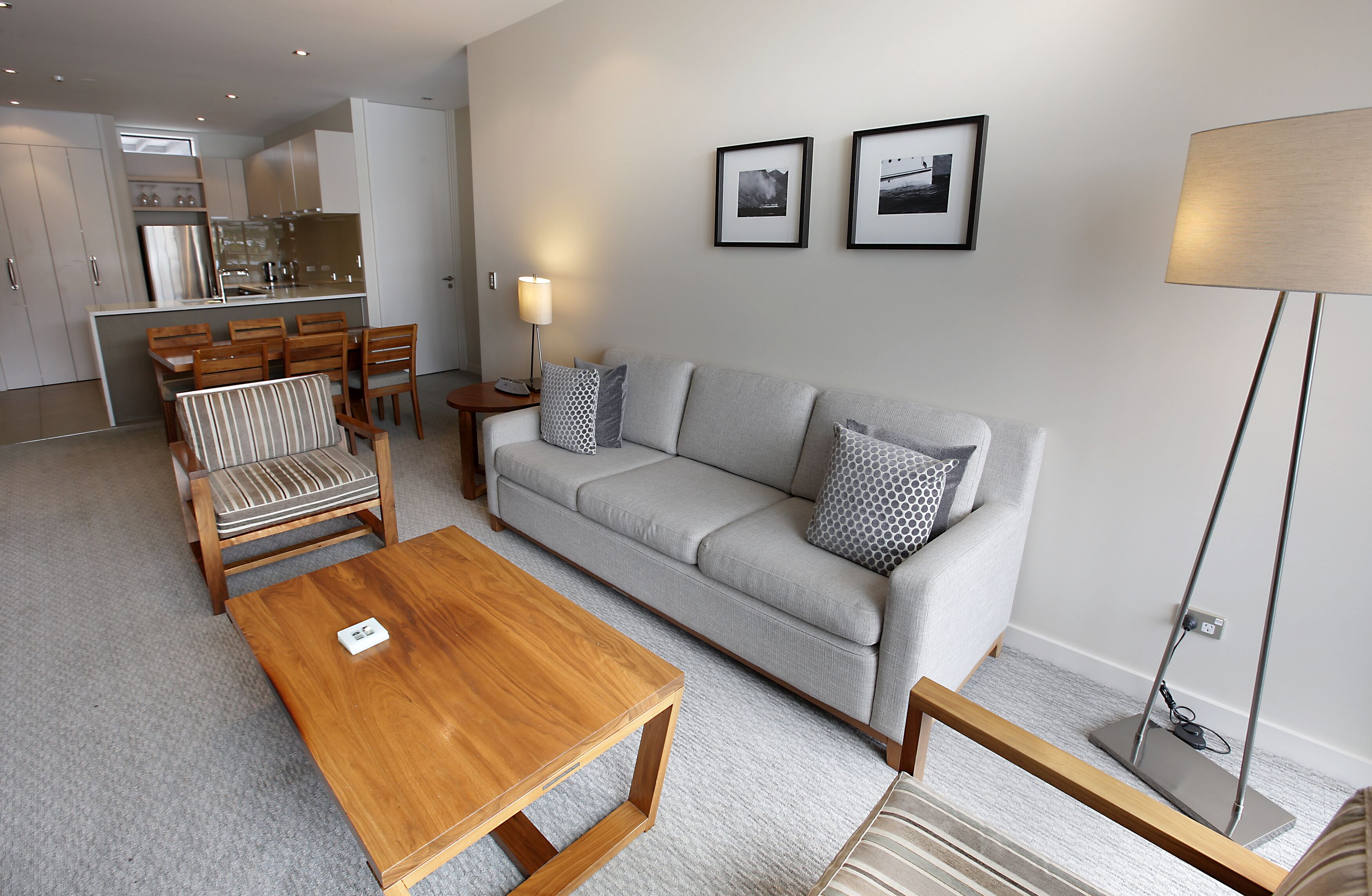 Un salón moderno con un sofá gris, una mesa de centro de madera y un sillón a rayas. Se ve una cocina al fondo.
