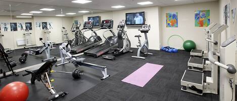 Une salle de sport équipée de tapis de course, de vélos elliptiques, d’appareils de musculation et de ballons d’exercice.