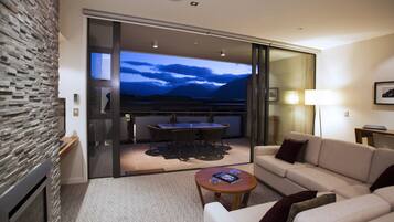 A modern hotel room with a stone wall, a sofa, a coffee table, and a balcony with a view of mountains.