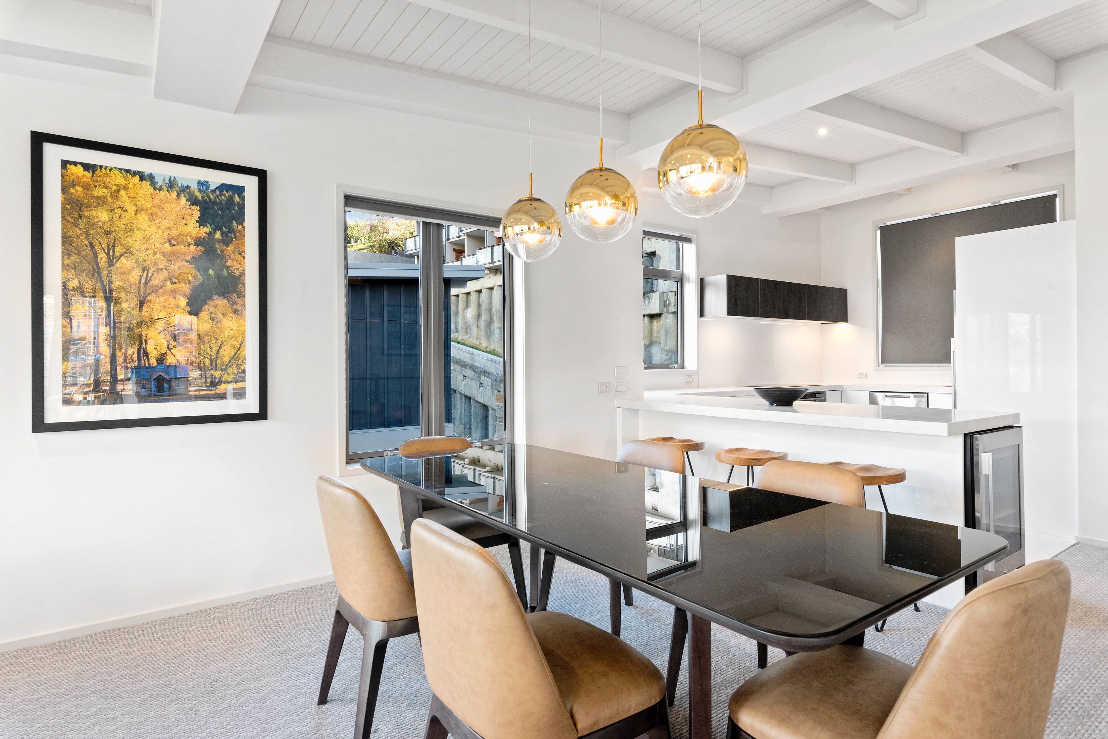 A modern dining area with a glass-top table, leather chairs, pendant lighting, and a framed picture on the wall.
