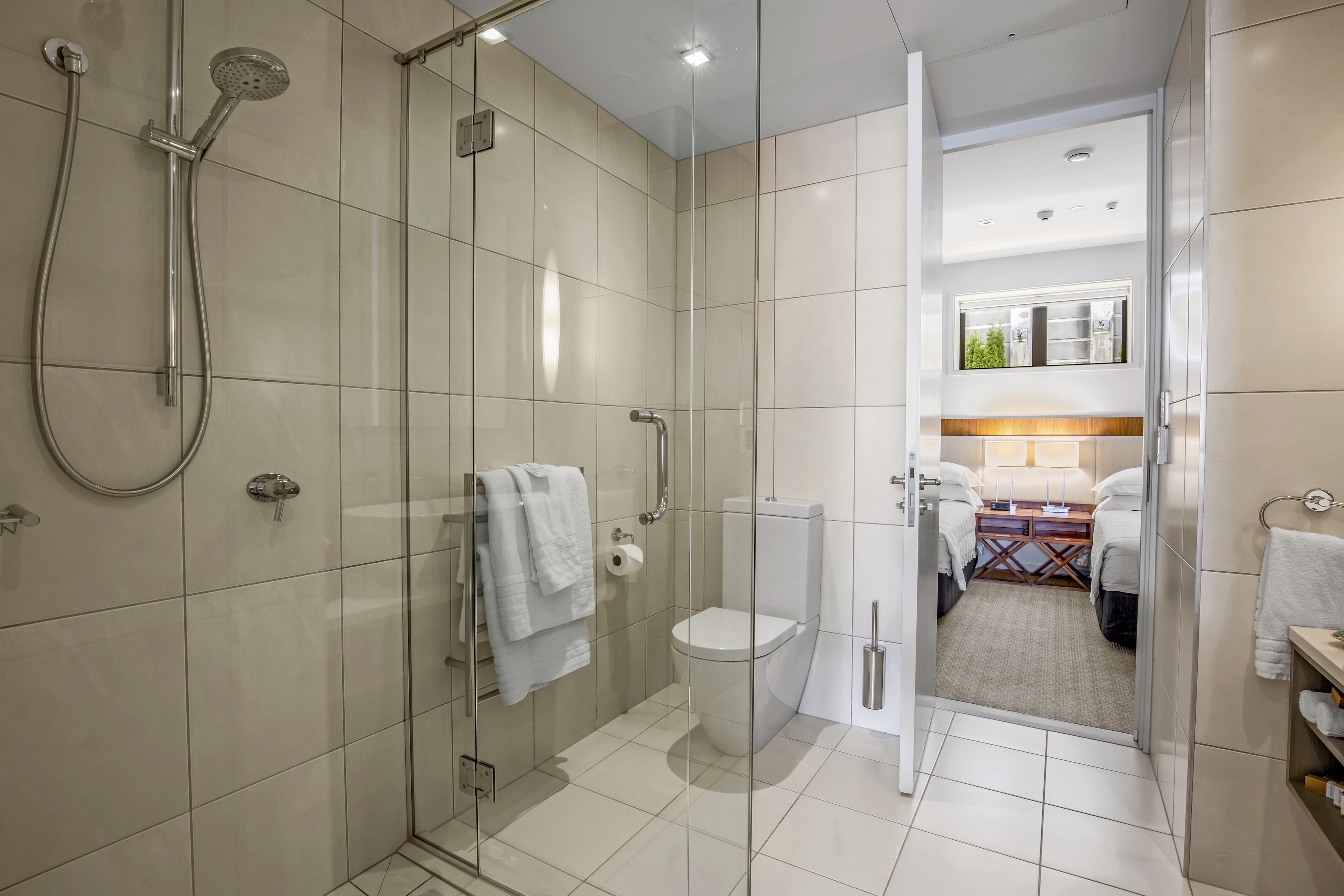 A modern bathroom with a glass-enclosed shower, a toilet, and a walk-in closet with a bed.