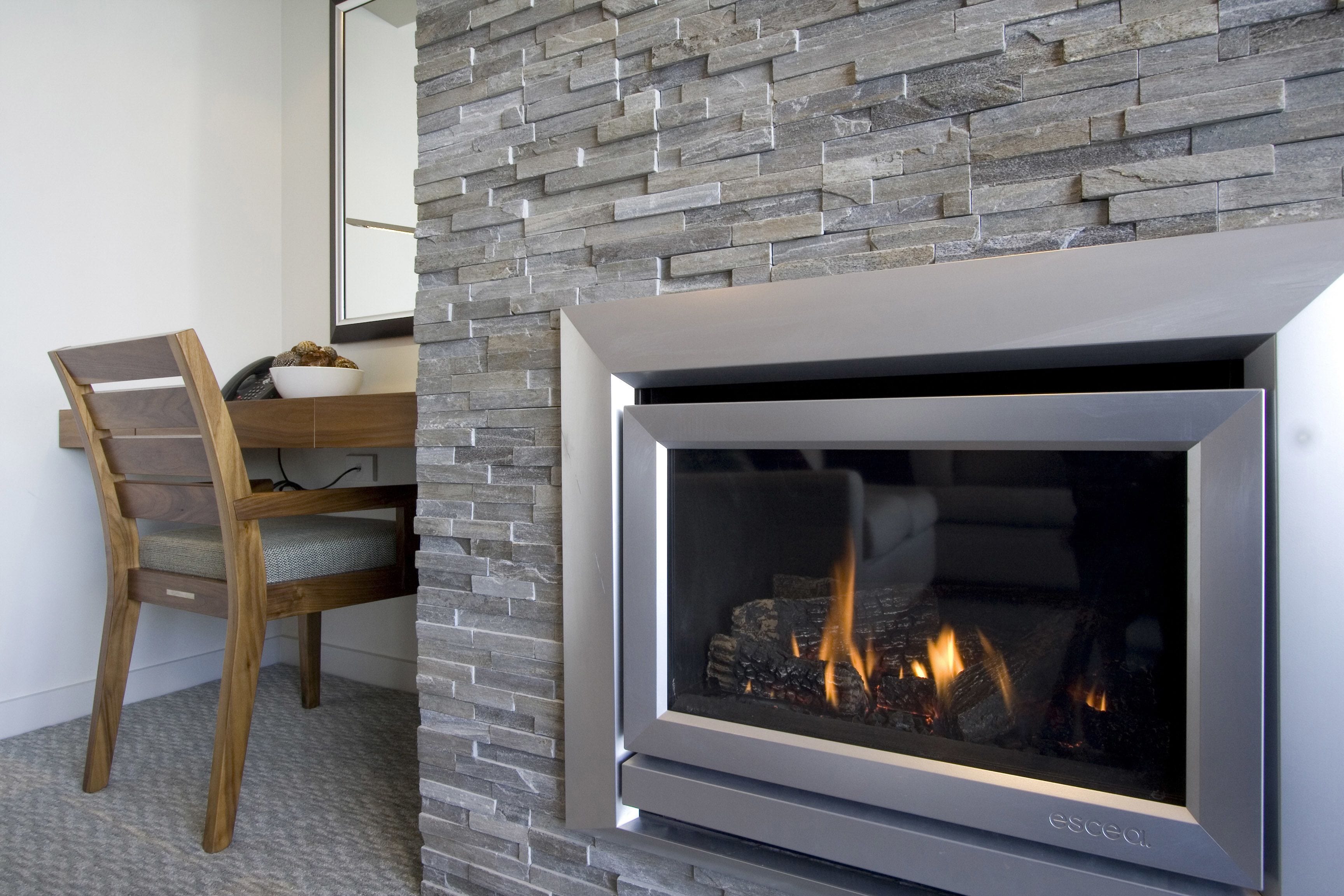 A modern fireplace with a stone facade, a wooden chair, and a dining table.