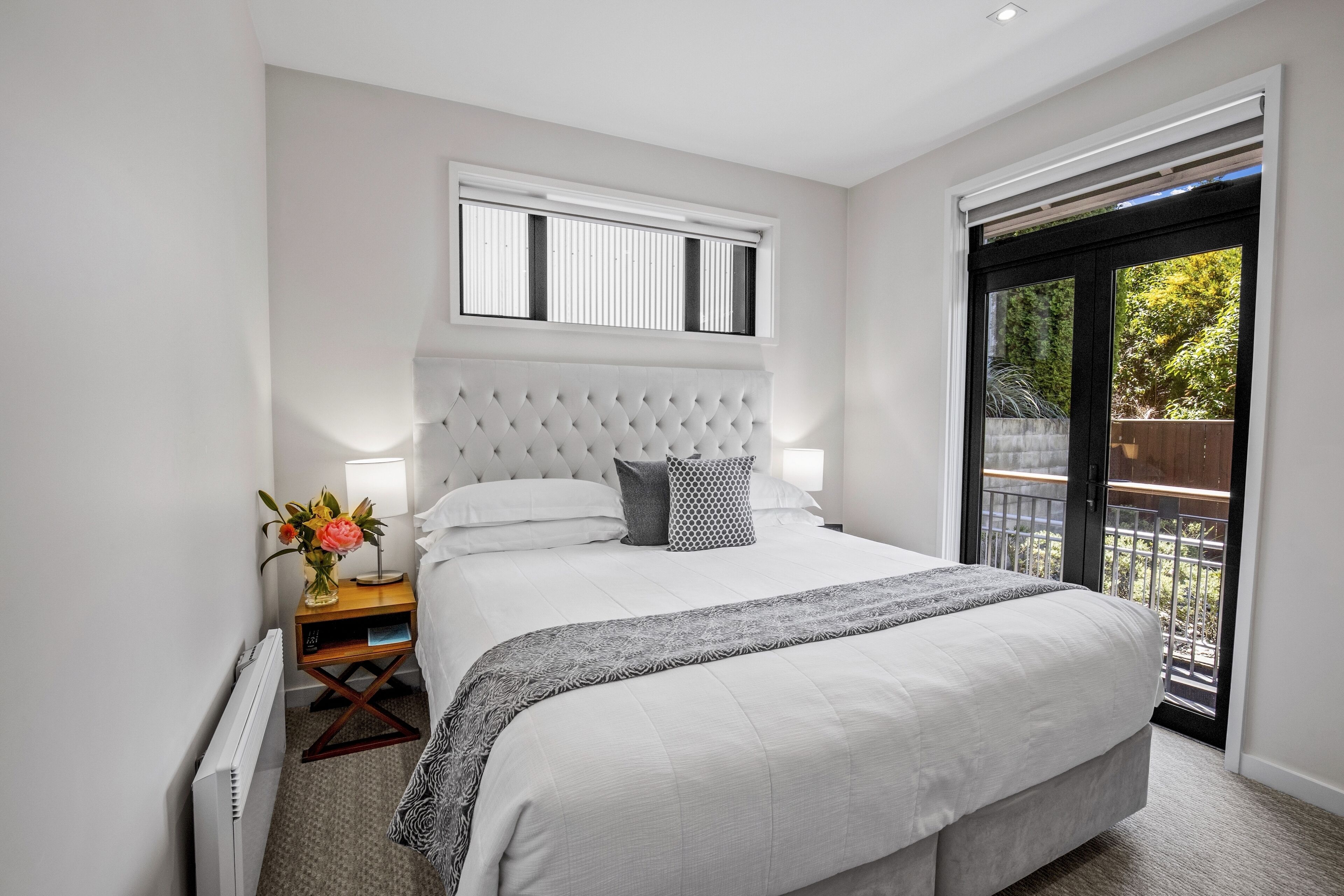Une chambre moderne avec un grand lit, une table de chevet, une lampe et une vue sur l’extérieur grâce à une porte coulissante.