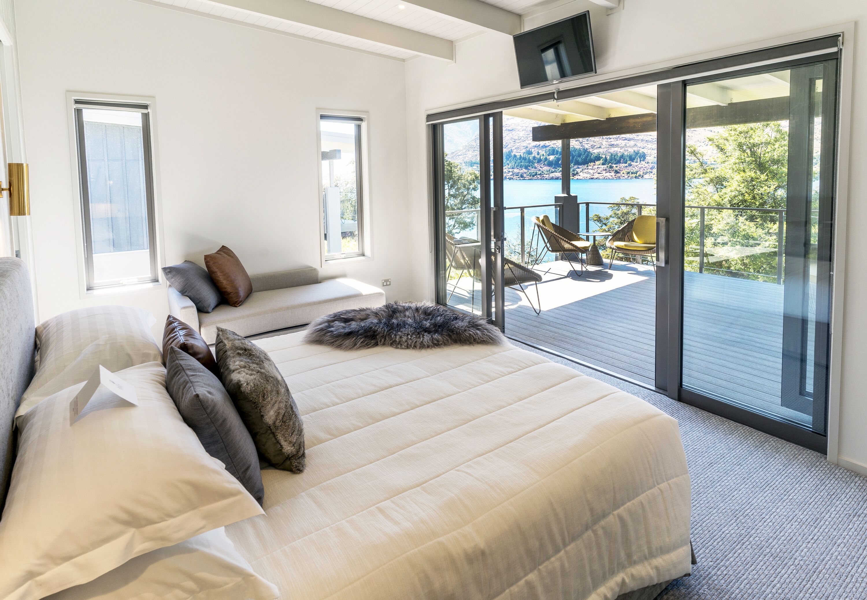 Un dormitorio con una cama grande, un sofá y un balcón con vistas a un lago y montañas.