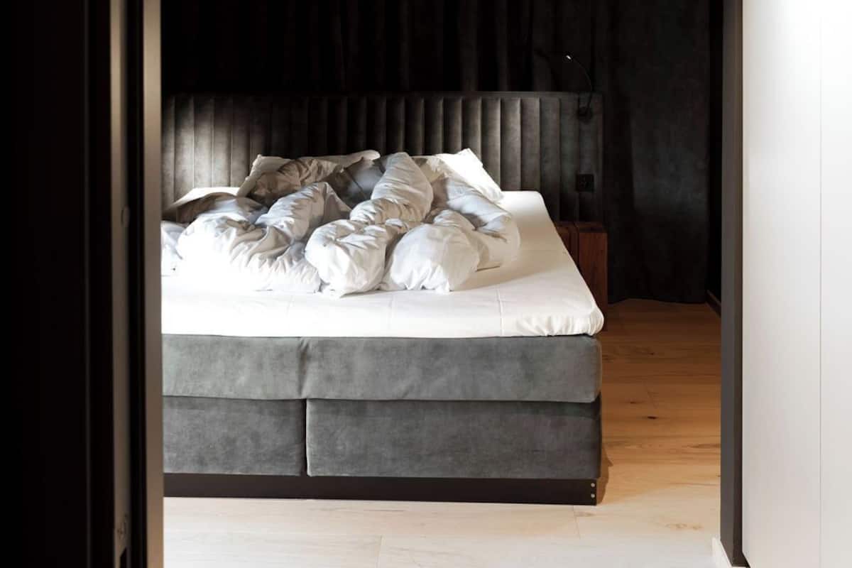Un dormitorio con cama, cortinas oscuras y suelo de madera.