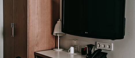 Habitación de hotel con armario de madera, escritorio con lámpara, televisor de pantalla plana, cafetera y teléfono.