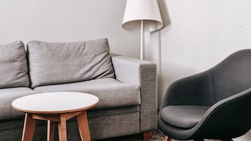 A living room with a grey sofa, a round wooden table, a black chair, and a white floor lamp.