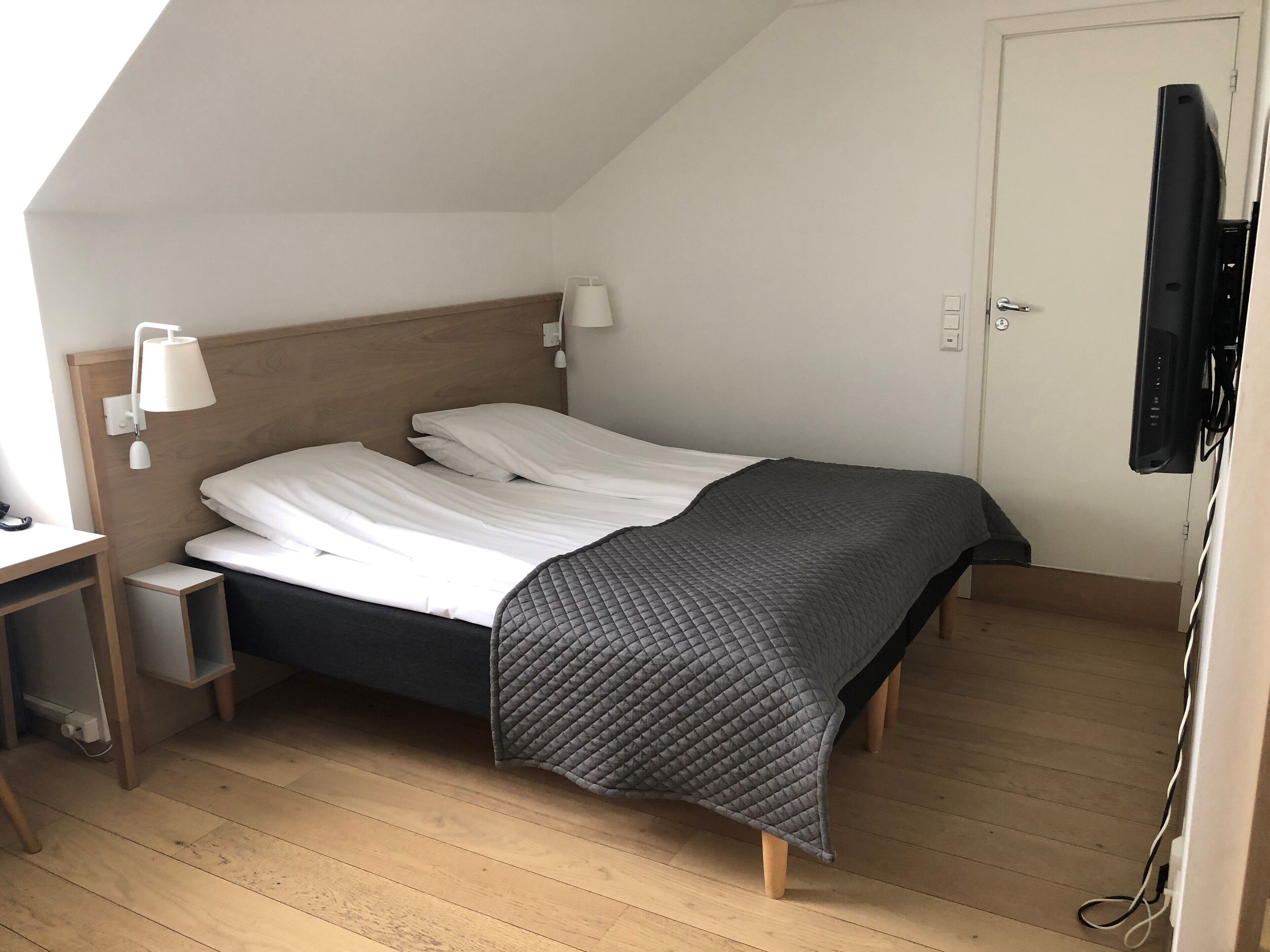 Une chambre à coucher avec un lit, des tables de chevet, un bureau, une télévision et une porte.