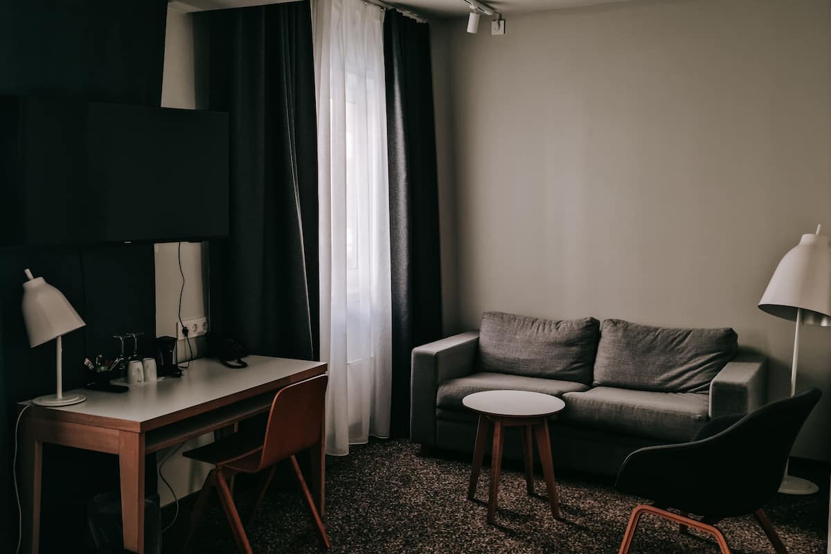 A modern hotel room with a desk, two chairs, a sofa, and a small round table.