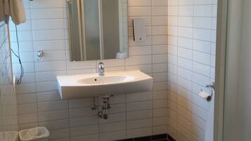 A bathroom with a white sink, mirror, and toilet. There is a towel hanging on the wall and a trash bin.