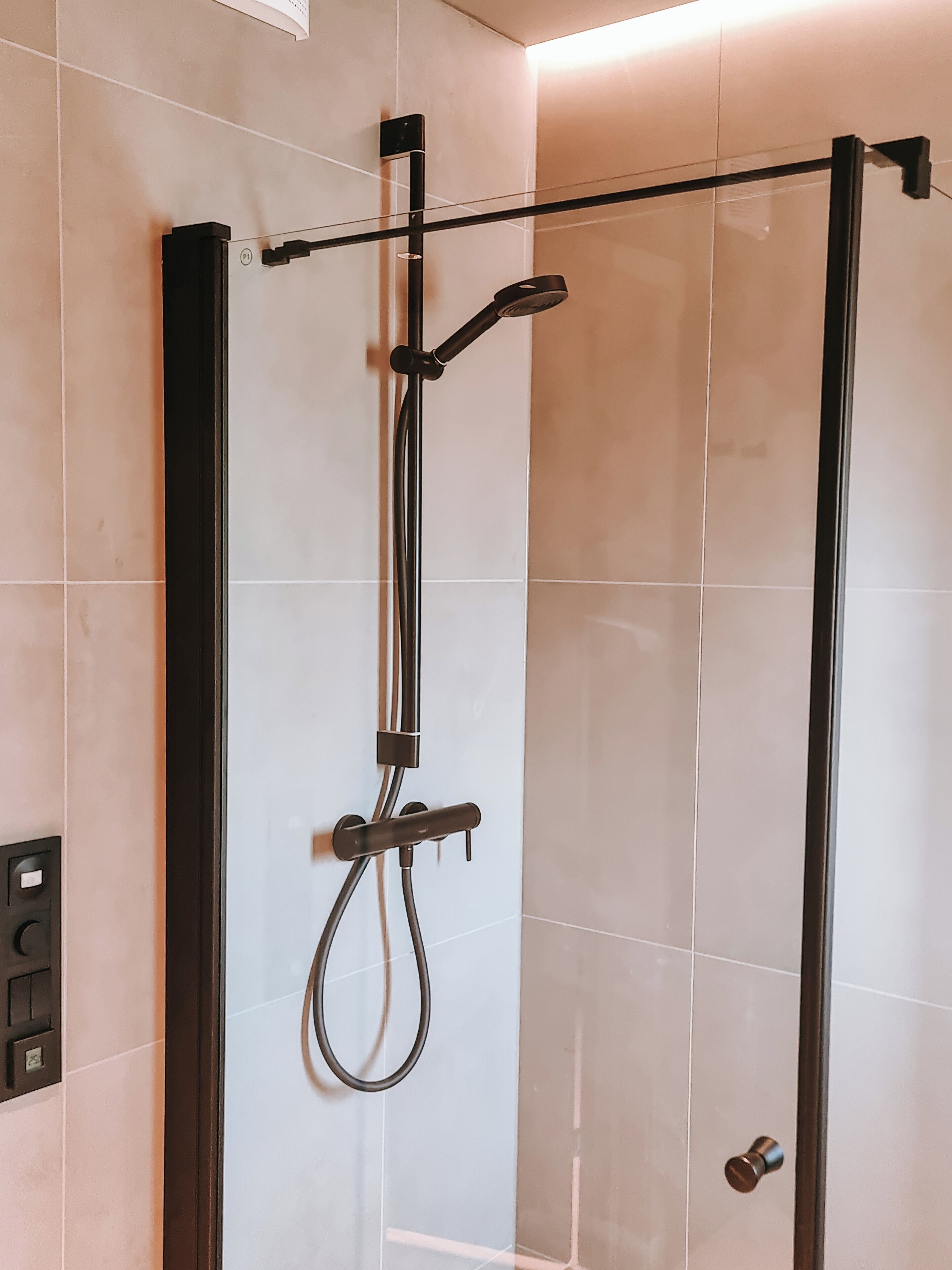 A modern shower enclosure with a control panel and a handheld showerhead.
