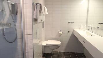 Et moderne badeværelse med en glasafskærmet brusekabine, et hvidt toilet og et stort spejl over en hvid vask.
