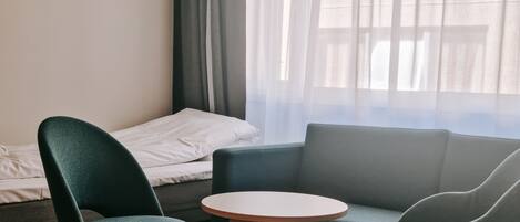 A room with a bed, a green armchair, a grey sofa, and a small round table.