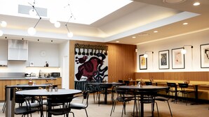 A modern dining area with round tables and black chairs, a wooden accent wall with a large abstract painting, and a ceiling with recessed lighting. - Hotel Noreg (Ålesund)