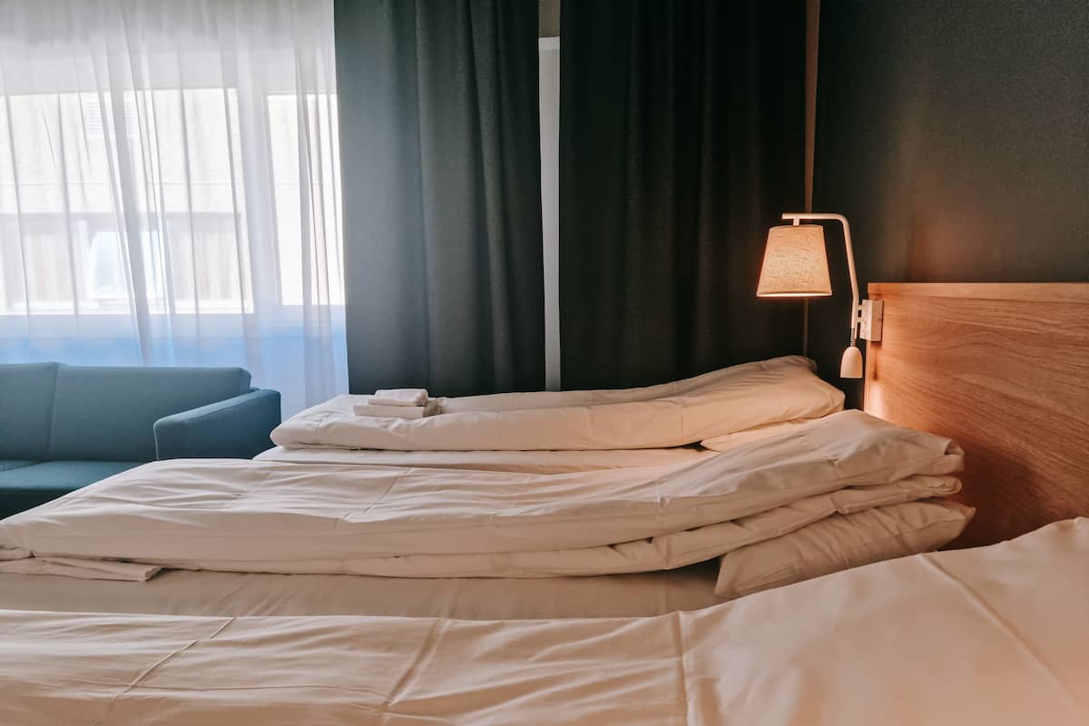A neatly made bed with white bedding, a wooden headboard, and a bedside lamp.