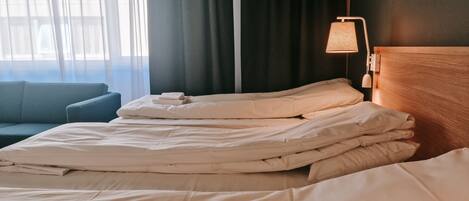 Un letto rifatto con cura, lenzuola bianche, una testiera in legno e una lampada da comodino.