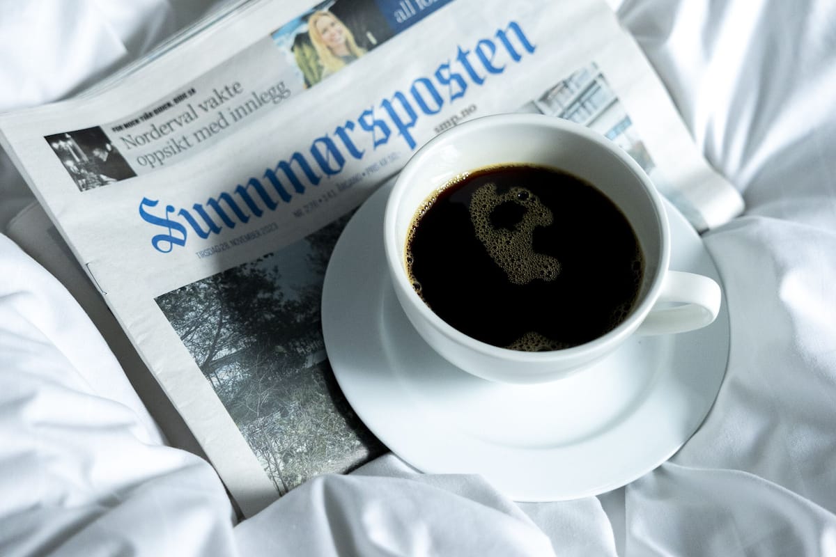 A newspaper with the headline "Summarsposten" and a cup of coffee on a bed.